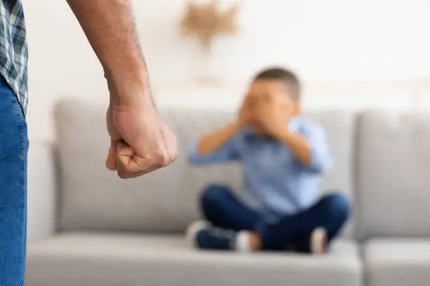 Child Abuse. Unrecognizable Black Father Clenching Fist Ready To Hit Scared Little Son Treatening Boy In Living Room At Home. Domestic Violence On Kid. Cropped, Selective Focus On Male Arm