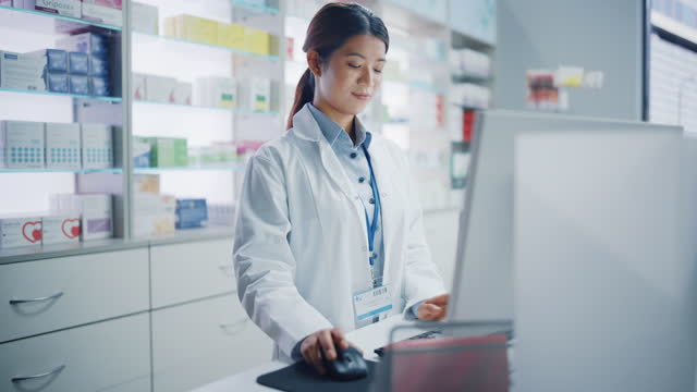 Pharmacy Drugstore: Beautiful Asian Pharmacist Uses Checkout Counter Computer, Does Inventory Checkup, Online Prescription of Medicine Packages, Drugs, Vitamin Boxes, Supplements, Health Care Products