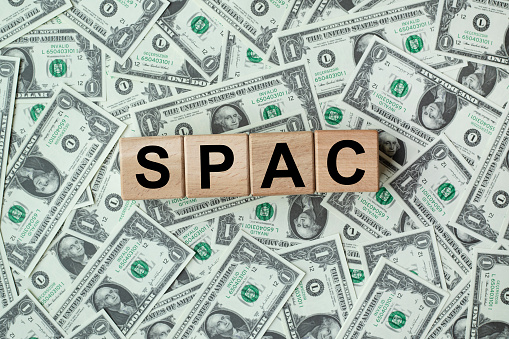 SPAC, special purpose acquisition company symbol. Wooden cubes with word 'SPAC' on beautiful background from dollar bills, copy space. Business and SPAC, special purpose acquisition company concept.