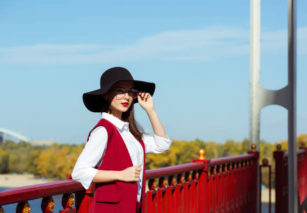 Romantic brunette model wearing red costume, hat and glasses, posing in a sunny day.  Space for text