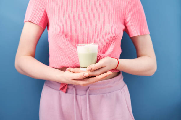 Woman holding cup of matcha latte at the blue wall background