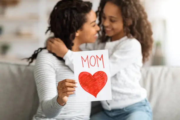 Photo of Cheerful black girl with gift card hugging her mom