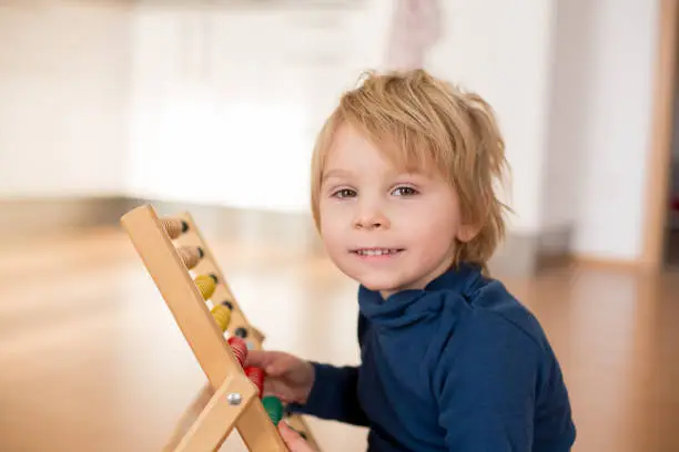 Sweet blond preschool child, toddler boy, playing with abacus at home,construction on the floor behing him