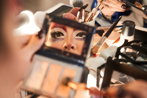 Reflexion at the hand mirror of the face of drag queen making bright makeup