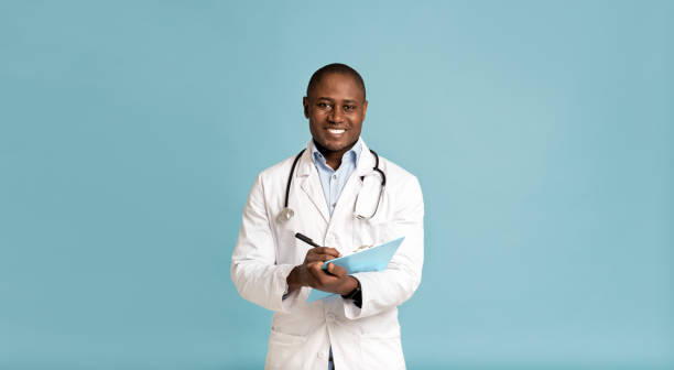 Good family doctor, therapist advice and friendly emotions of person Good family doctor, therapist advice and friendly emotions of person. Happy adult african american man in white coat with stethoscope makes notes in tablet, isolated on blue background, panorama drawing board stock pictures, royalty-free photos & images