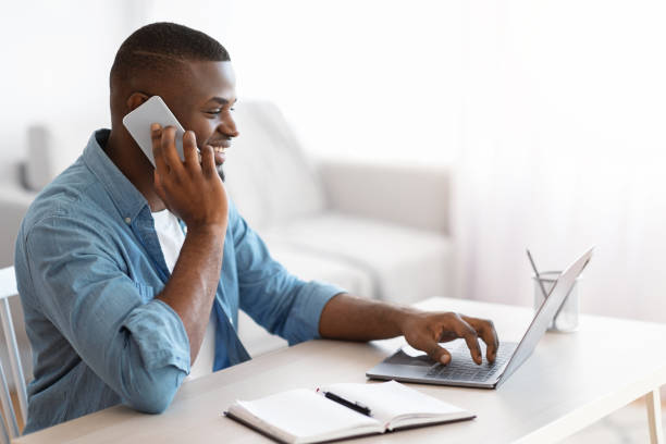 istock Work From Home. Smiling Black Freelancer Guy Using Laptop And Cellphone 1309255502