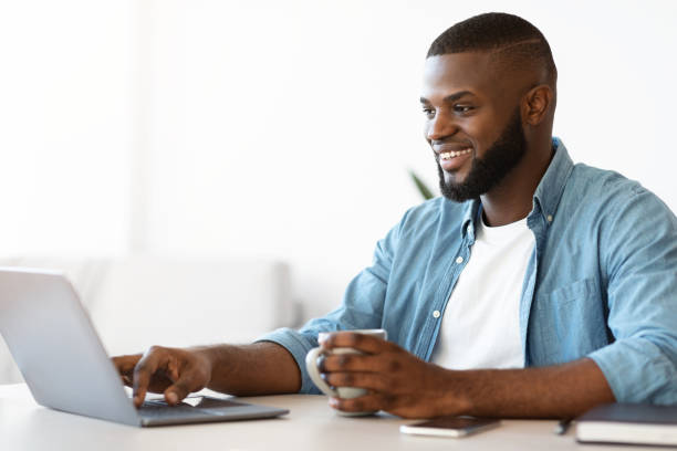 istock Freelancing Concept. Cheerful Black Freelancer Man Drinking Coffee And Working On Laptop 1309255505