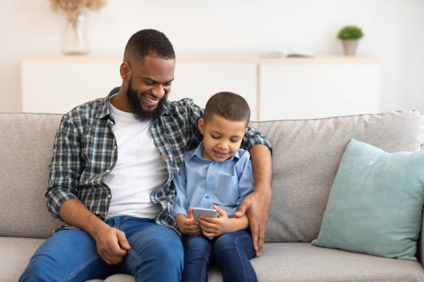 istock Black Boy And Dad Using Phone Playing Games Online Indoor 1309256482