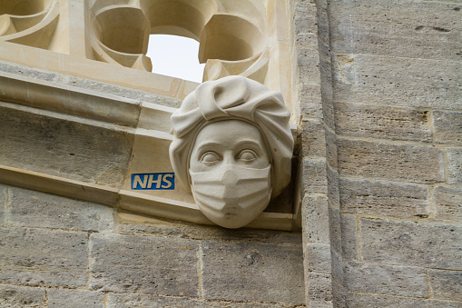 Christchurch, England – March 26 2021: New stone carving of a masked PPE NHS Worker commemorating or celebrating the Covid 19 Pandemic NHS work, landscape on Christchurch Priory, Dorset.