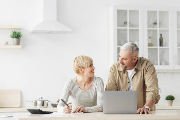 미소 짓는 선임 부부 배우자는 노트북, 계산기, 온라인 은행 청구서를 지불하는 새로운 기술을 사용합니다. - senior adult couple computer retirement 뉴스 사진 이미지