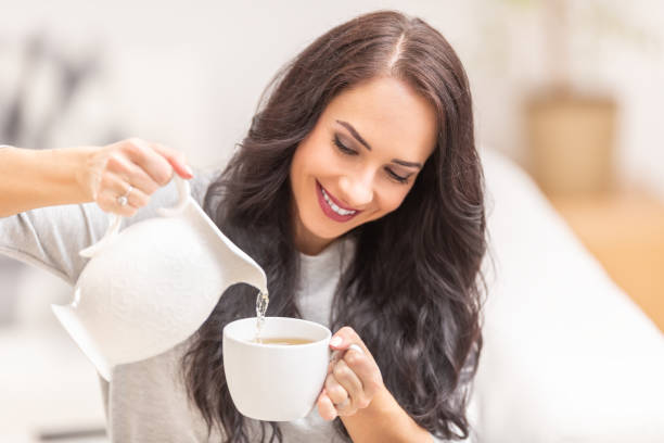 istock Dark curly haired woman pouring hot coffee or tea into white cup. 1309257016