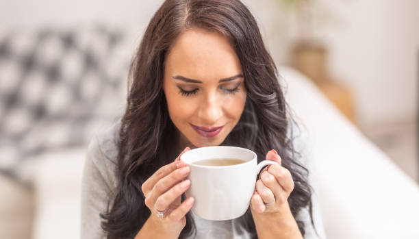 若いブルネットの女性は、お茶やコーヒーを一杯持って、素敵な香りを嗅ぎます。 - コーヒー　淹れる ストックフォトと画像
