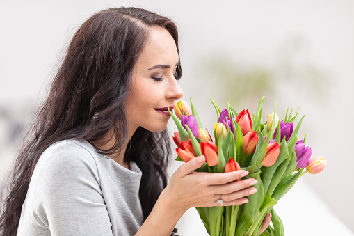 Dark haired woman smelling lovely aroma of fresh colorful tulips.