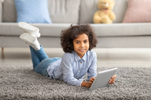 istock Black girl using digital tablet, lying on the floor carpet 1309257174