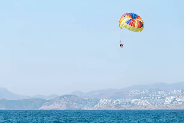 Photo of Couple under multicolored parachute hanging mid air. Positive human emotions, feelings, travel, vacation.