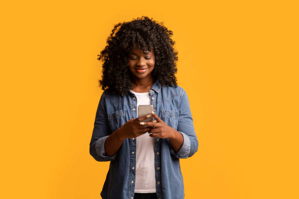 istock Happy black lady using modern smartphone on yellow 1309259568