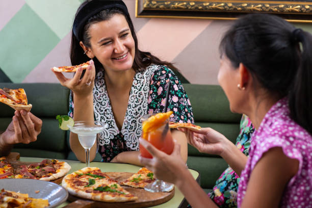 istock Two young multiethnic girlfriends eating, talking and laughing in restaurant or cafe during summer 1309260823