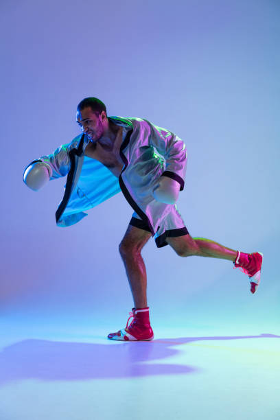 istock High-fashion styled man in white outfit pacticing box isolted over gradient background in neon light 1309260947