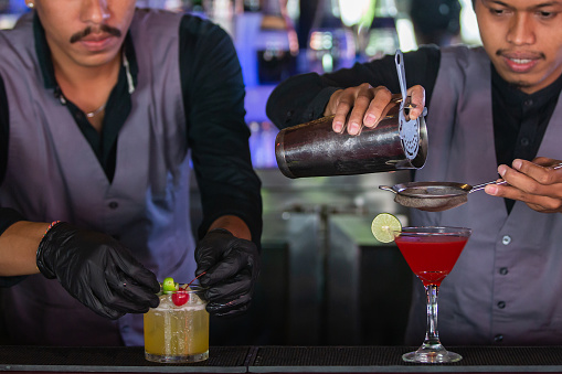 Two expert bartenders are making cocktails at night club or bar