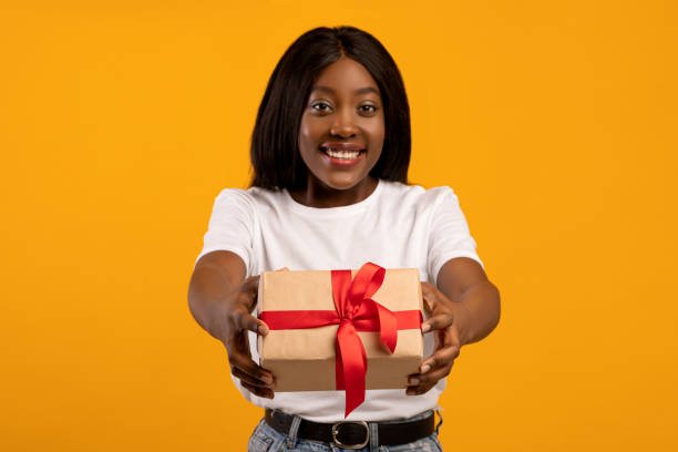 istock Cheerful black lady outstretching present, yellow background 1309262265