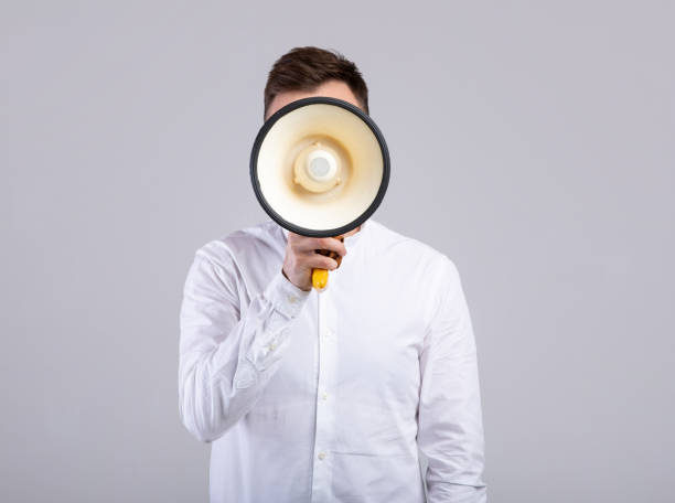 istock Faceless young businessman hiding behind megaphone on grey studio background. Public announcement or advertisement 1309262288