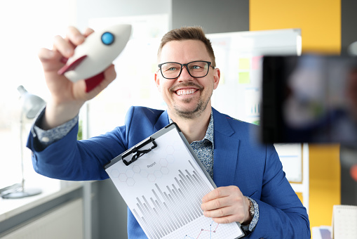 Smiling man holding rocket and business charts in his hand. Rules for building a successful business concept