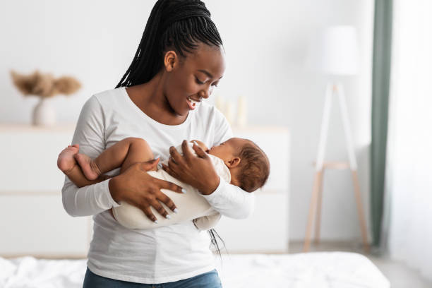 African American mother singing lullaby for infant to sleep Maternity Concept. Portrait of smiling African American woman holding her adorable small black upset baby on hands, singing lullaby to sleep, comforting infant kid standing in bedroom at home the mom song stock pictures, royalty-free photos & images