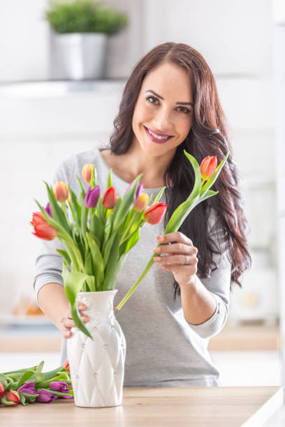 dark haired woman putting fresh colorful tulips into white vase. - tulip vase flower spring imagens e fotografias de stock
