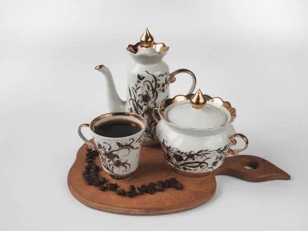 A cup of coffee, beans with coffee pot and sugar-bowl on a wood board, a white background. Dishes for coffee in a retro style.