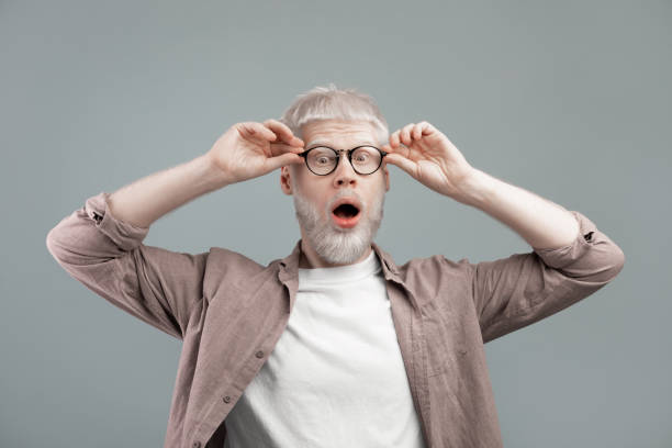 istock Surprised albino blond man touching glasses with open mouth, guy posing over grey studio background 1309264421