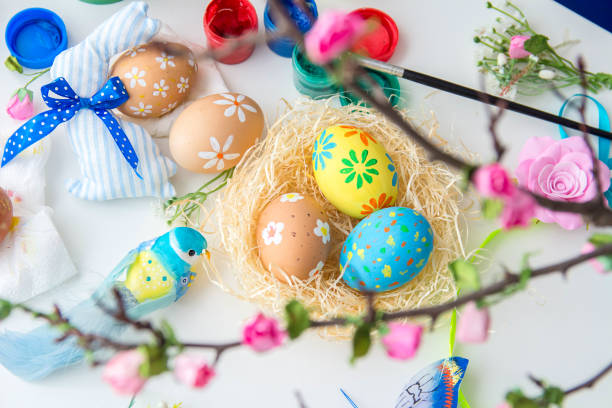 istock Multicolored easter painted handmade eggs in bird's nest, easter decorations, paints and brushes on white table. Festive Easter background. 1309264534