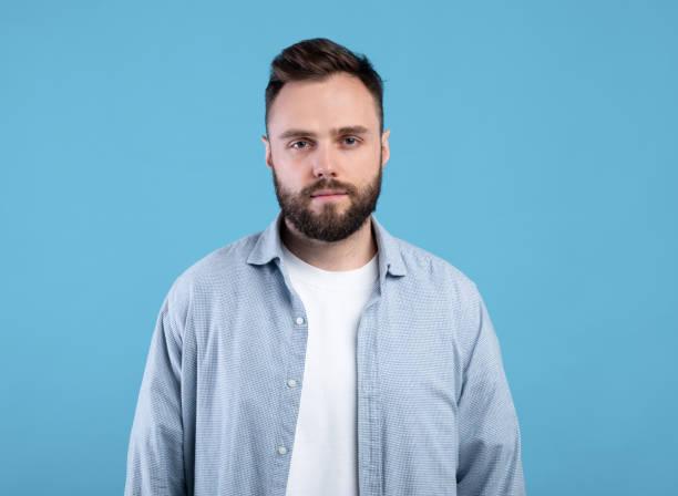 istock Portrait of serious young guy looking at camera on blue studio background 1309265239