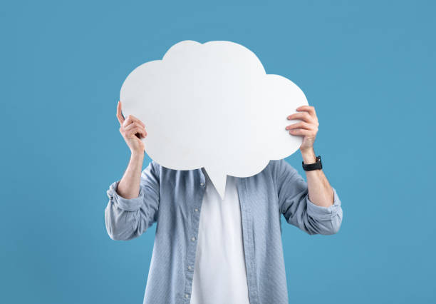 Faceless young man covering his face with speech bubble on blue studio background, mockup for design