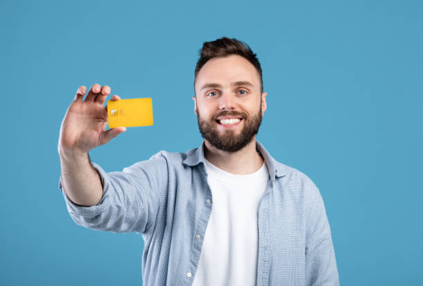 istock Positive millennial guy showing credit card and smiling on blue studio background 1309265324