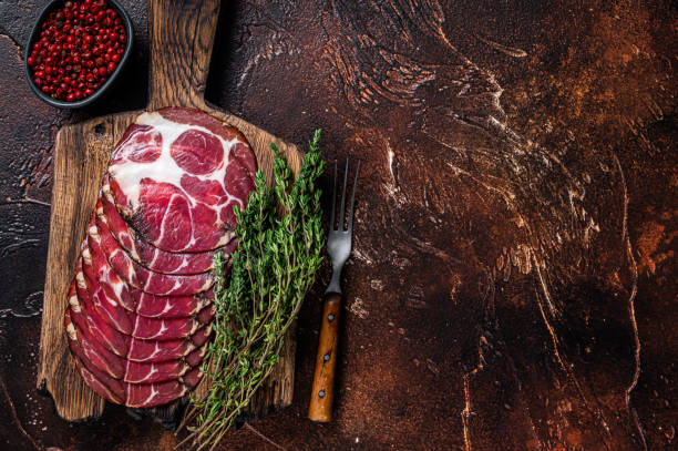 istock Sliced cured coppa ham  on wooden board with thyme. Dark background. Top view. Copy space 1309265347