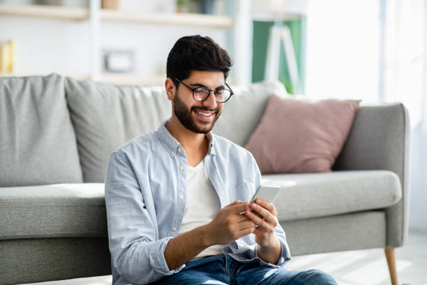 istock Arab guy texting and browsing internet on smartphone, resting at home, leaning on sofa 1309265575