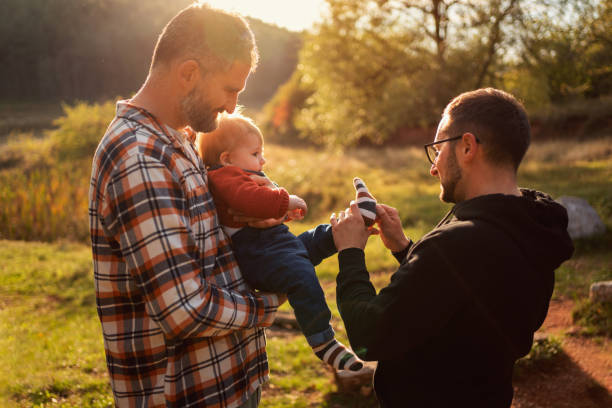 Loving gay couple with their baby boy Gay couple with their child in nature, fixing baby socks to their son. homosexual stock pictures, royalty-free photos & images