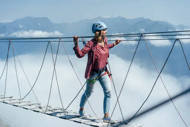 Photo of A happy woman walks on a suspension bridge high in the mountains at the level of a cloud.