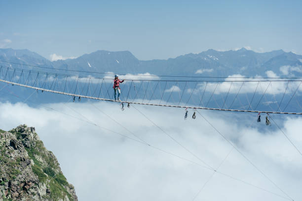A person walks on a suspended rope bridge in the clouds. A person walks on a suspended rope bridge in the clouds. Extreme attraction. Wanderlust and adventures. sochi photos stock pictures, royalty-free photos & images