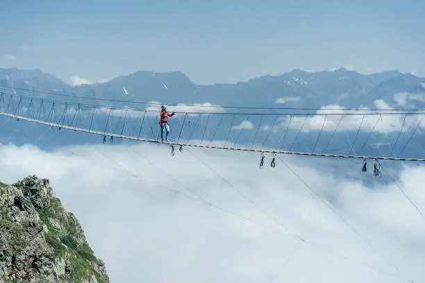 Photo of A person walks on a suspended rope bridge in the clouds.