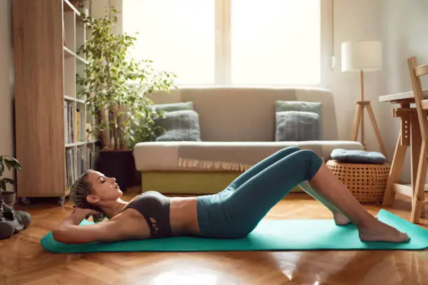 Photo of Side view of a woman in sportswear practicing at home on her mat
