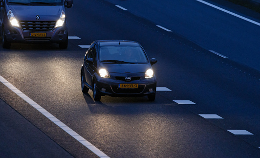 Wierden, Overijssel, Netherlands, july 20th 2016, Dutch grey 2010 city car Toyota Aygo driven by a female adult at sunset on the dutch highway A35 at Wierden, another vehicle is driving right behind, seen from a viaduct - the A35 is a 2-lane motorway connecting Enschede with Wierden