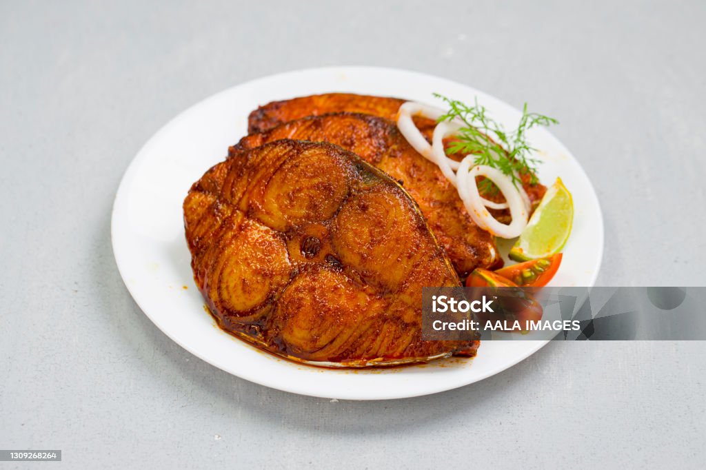 Seer fish fry Seer fish fry arranged beautifully and garnished with onion, lemon and tomato slices on white ceramic plate with grey textured background. Fish Stock Photo