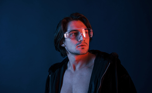 Beautiful long haired hot man in glasses is in the studio with blue neon lighting.