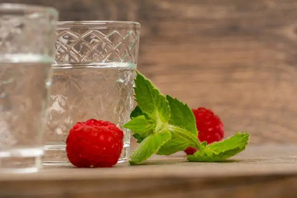vodka in shot glass with raspberry and mint on aged wooden table
