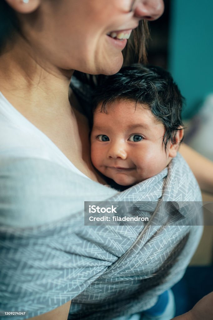 Baby is always close to mom Close-up shot of a mother carrying her cute baby in a sling Baby Carrier Stock Photo