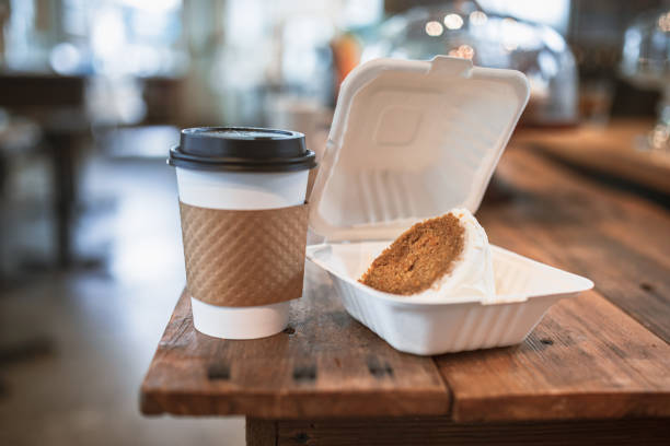 A rich and spicy slice of moist carrot cake with cream cheese frosting pictured on a white to-go container, a cup of coffee to go along with it.