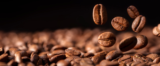 Coffee beans falling into a heap on dark background with copy space