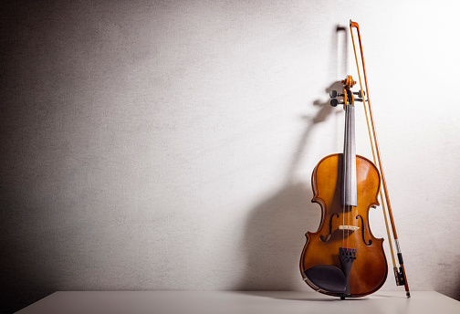 Violin leaning against a blank white textured wall  background with copy space for music concept