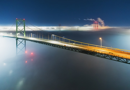 A night time aerial drone view of the MacKay bridge spanning Halifax harbour. A fog bank enshrouds the area.